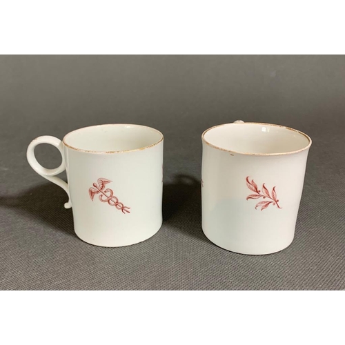 152 - Two possibly Capodimonte or Naples coffee cups with the Caduceus symbol and sparse floral decoration... 