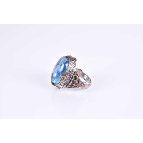 343 - An unusual silver and blue glass ring, set with an oval blue glass cabochon, of stylised naturalisti... 