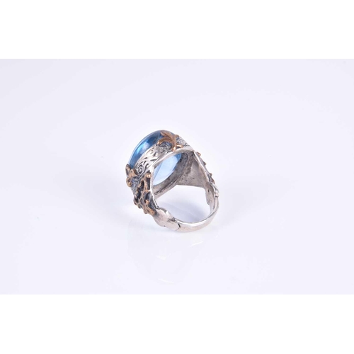 343 - An unusual silver and blue glass ring, set with an oval blue glass cabochon, of stylised naturalisti... 