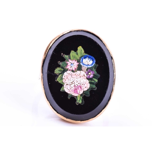 653 - A yellow metal and micro mosaic ring, the black onyx mount inlaid with a floral design, shank unmark... 