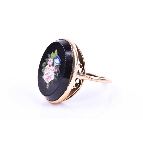 653 - A yellow metal and micro mosaic ring, the black onyx mount inlaid with a floral design, shank unmark... 