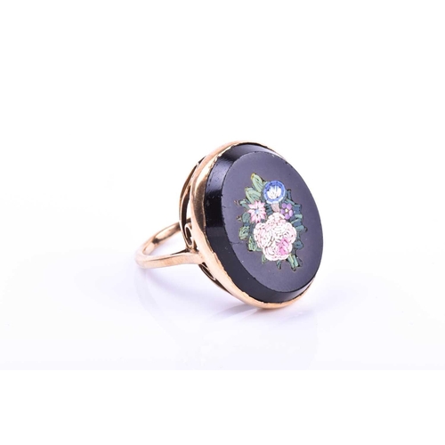 653 - A yellow metal and micro mosaic ring, the black onyx mount inlaid with a floral design, shank unmark... 