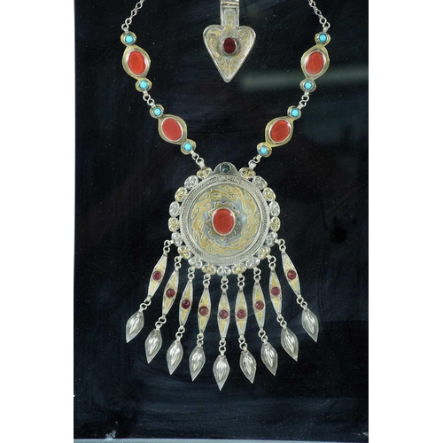 779 - An Eastern white metal necklace, set with assorted hardstones, mounted and framed, the frame 69 cm h... 