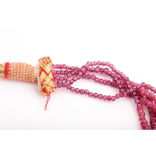 182 - A five strand ruby necklace, comprised of smooth and faceted rubies, with red and gold fabric adjust... 