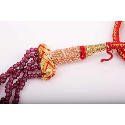 182 - A five strand ruby necklace, comprised of smooth and faceted rubies, with red and gold fabric adjust... 