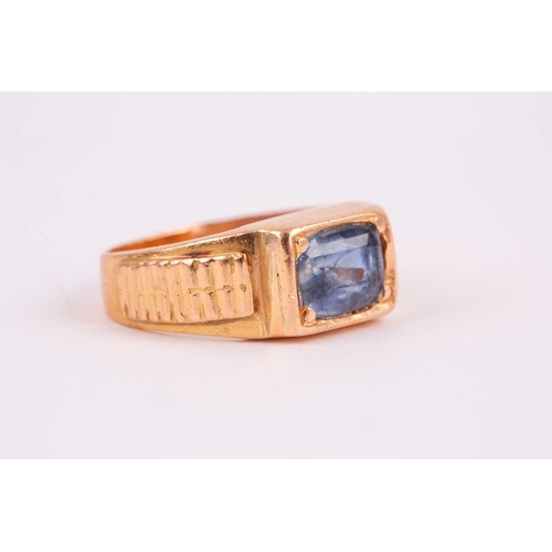 27 - A yellow metal and sapphire ring, set east to west with a mixed rectangular-cut sapphire, the stone ... 