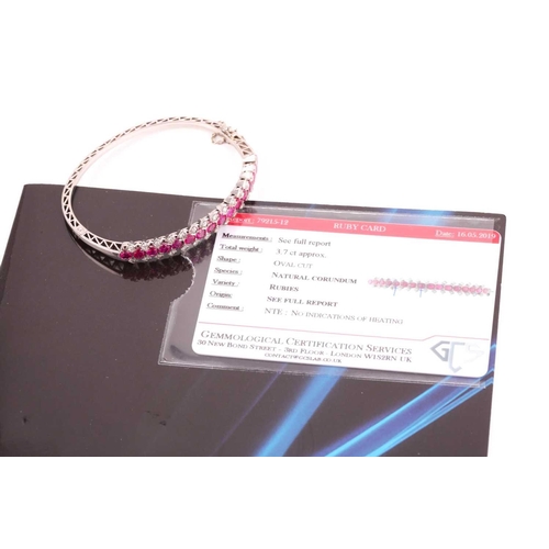 28 - A ruby and diamond half hoop bangle; the front set with sixteen oval cut rubies, with a divided band... 