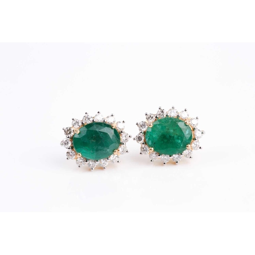 33 - A pair of emerald and diamond cluster earrings, the mixed oval-cut emerald in four claw mount above ... 