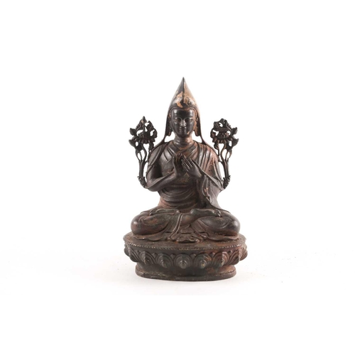 87A - A Tibetan patinated and gilt bronze figure of a Gelpuga Lama seated with flowers about his arms and ... 