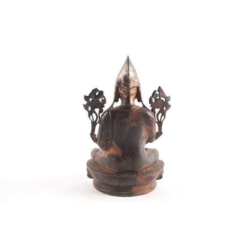 87A - A Tibetan patinated and gilt bronze figure of a Gelpuga Lama seated with flowers about his arms and ... 