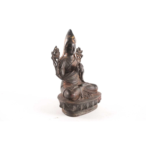 87A - A Tibetan patinated and gilt bronze figure of a Gelpuga Lama seated with flowers about his arms and ... 