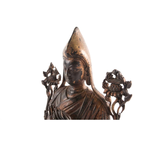 87A - A Tibetan patinated and gilt bronze figure of a Gelpuga Lama seated with flowers about his arms and ... 