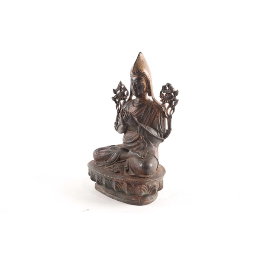 87A - A Tibetan patinated and gilt bronze figure of a Gelpuga Lama seated with flowers about his arms and ... 