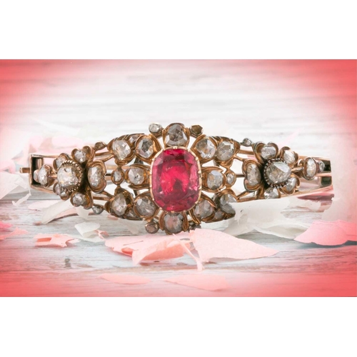 72 - An antique yellow metal and diamond bangle, set with a reddish pink central stone, likely spinel, th... 