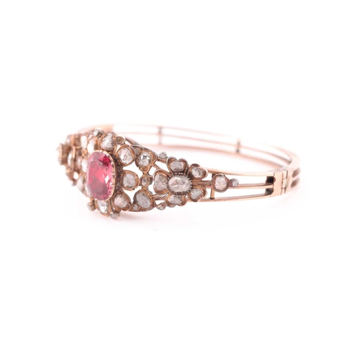 72 - An antique yellow metal and diamond bangle, set with a reddish pink central stone, likely spinel, th... 