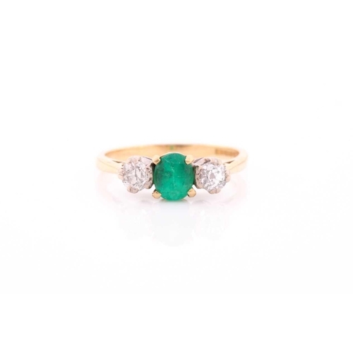 87 - A three stone half hoop emerald and diamond ring. The oval cut emerald in four claw mount flanked by... 