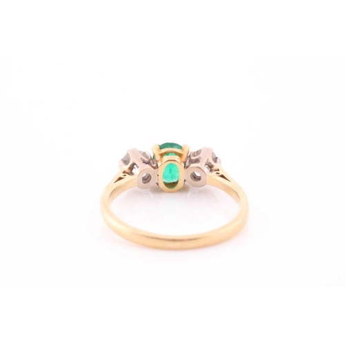 87 - A three stone half hoop emerald and diamond ring. The oval cut emerald in four claw mount flanked by... 