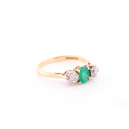 87 - A three stone half hoop emerald and diamond ring. The oval cut emerald in four claw mount flanked by... 