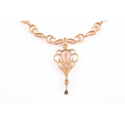 219 - An Indian diamond set necklace; the centre with a diamond set scrolling, openwork drop, from a circu... 