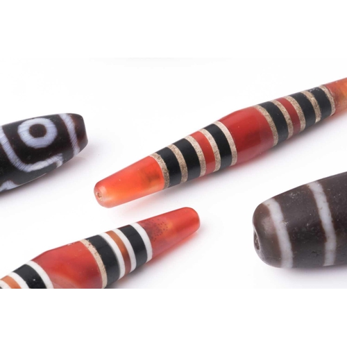 154 - A collection of five Tibetan carved agate Dzi beads of turned elliptical form, some with banded and ... 