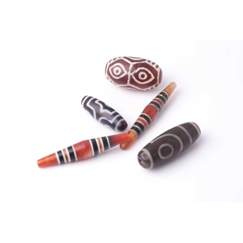 154 - A collection of five Tibetan carved agate Dzi beads of turned elliptical form, some with banded and ... 