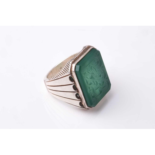 357 - An Eastern white metal gentleman's ring set with a canted rectangular green hardstone panel intaglio... 