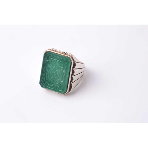 357 - An Eastern white metal gentleman's ring set with a canted rectangular green hardstone panel intaglio... 