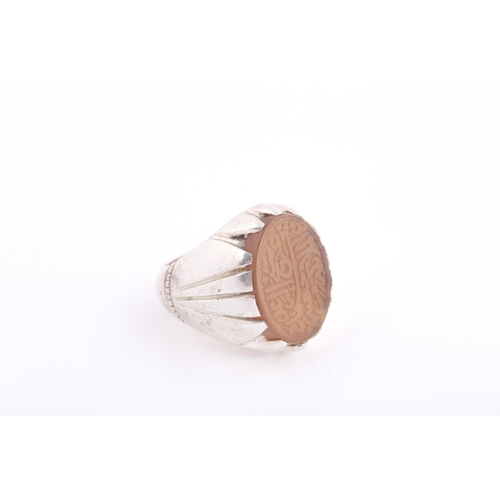 252 - An Indo Persian white metal and hardstone ring, set with a pale orange onyx hardstone with engraved ... 