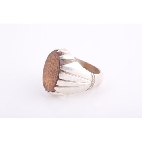 252 - An Indo Persian white metal and hardstone ring, set with a pale orange onyx hardstone with engraved ... 