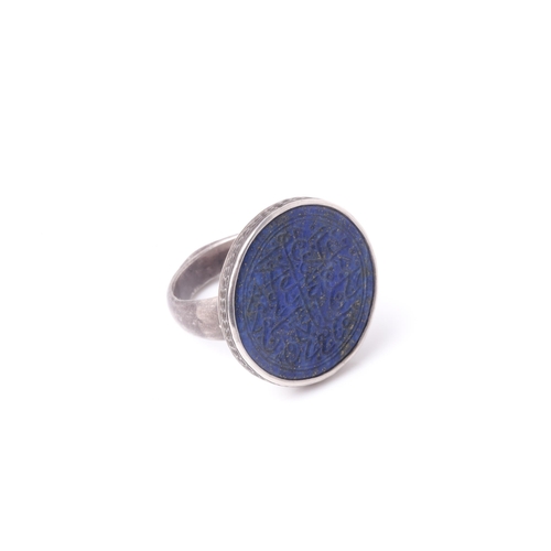 255 - A probably Persian white metal dress ring set with a circular lapis lazuli panel engraved with Islam... 