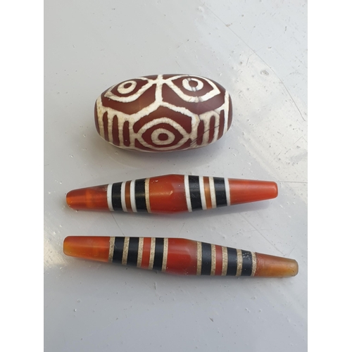 94 - A collection of five Tibetan carved agate Dzi beads of turned elliptical form, some with banded and ... 