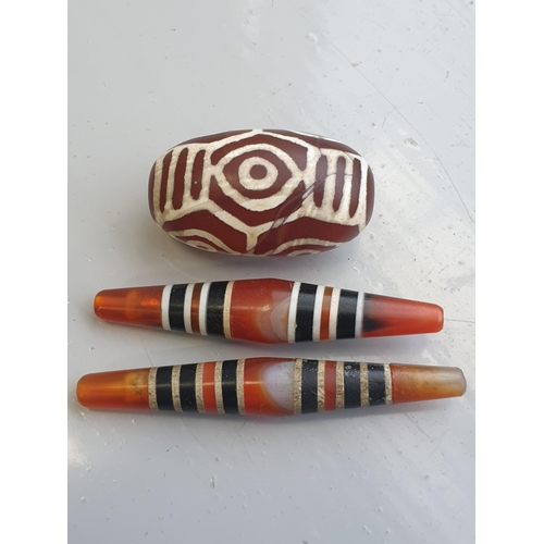 94 - A collection of five Tibetan carved agate Dzi beads of turned elliptical form, some with banded and ... 