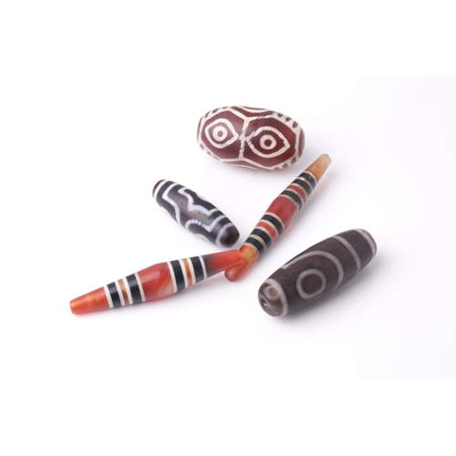 94 - A collection of five Tibetan carved agate Dzi beads of turned elliptical form, some with banded and ... 