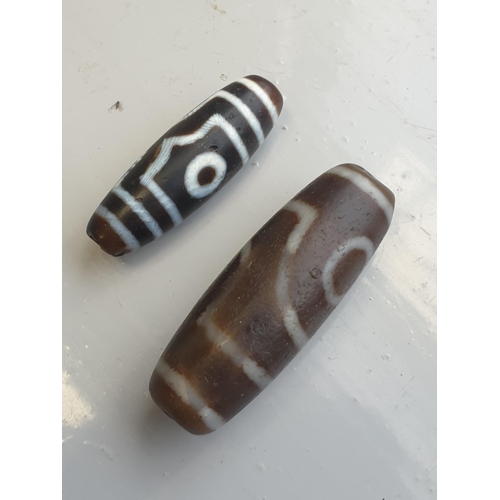 94 - A collection of five Tibetan carved agate Dzi beads of turned elliptical form, some with banded and ... 