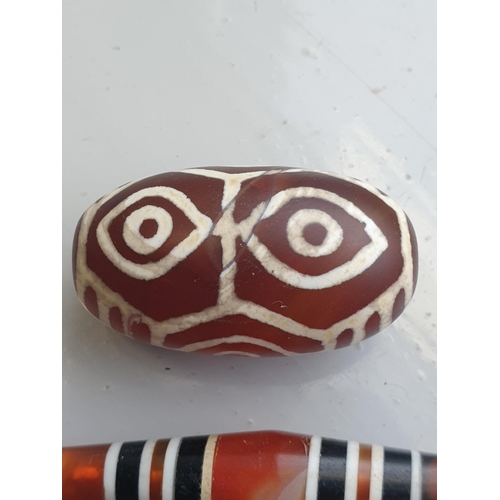 94 - A collection of five Tibetan carved agate Dzi beads of turned elliptical form, some with banded and ... 