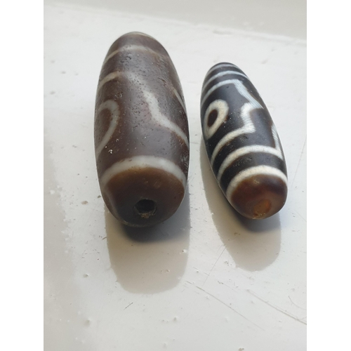 94 - A collection of five Tibetan carved agate Dzi beads of turned elliptical form, some with banded and ... 