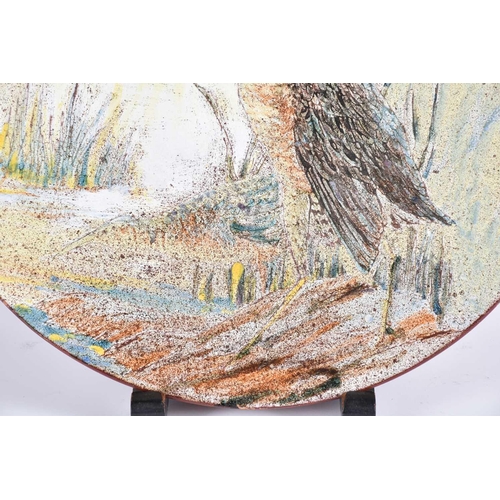 497 - A large Chelsea Pottery terracotta charger, painted with a wading bird by reeds and a stream, incise... 