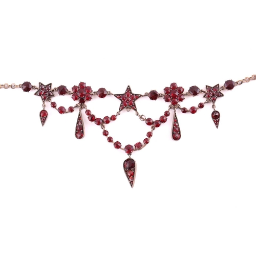 1 - A garnet and red paste garland necklace in gilt metal, with florets, five-pointed stars and teardrop... 