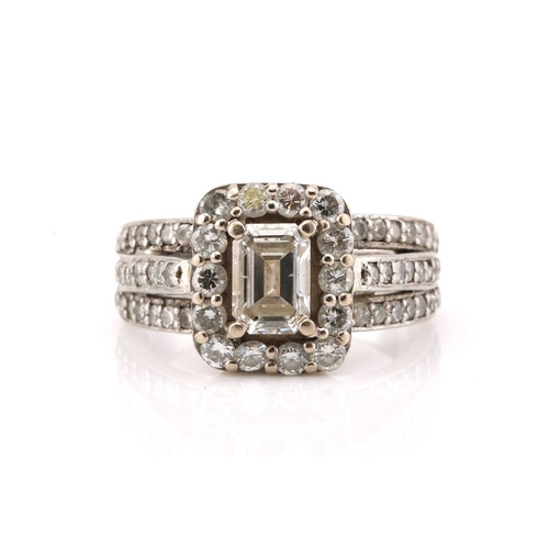 112 - A platinum and diamond entourage ring, featuring an emerald cut diamond in the centre with an approx... 