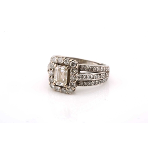 112 - A platinum and diamond entourage ring, featuring an emerald cut diamond in the centre with an approx... 