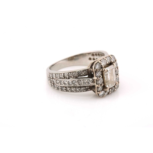 112 - A platinum and diamond entourage ring, featuring an emerald cut diamond in the centre with an approx... 