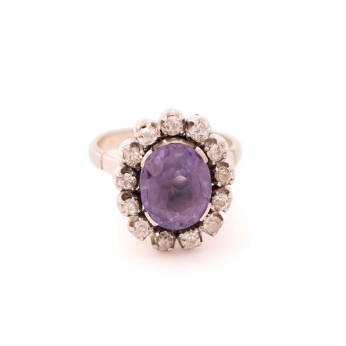 83 - A synthetic colour-changing sapphire and diamond cluster ring, centred with an oval cut synthetic co... 