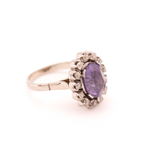 83 - A synthetic colour-changing sapphire and diamond cluster ring, centred with an oval cut synthetic co... 