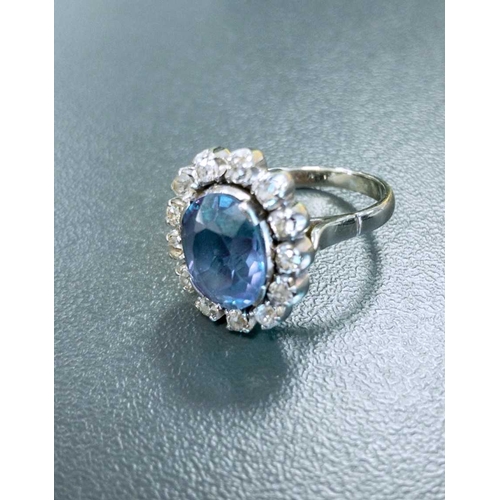 83 - A synthetic colour-changing sapphire and diamond cluster ring, centred with an oval cut synthetic co... 