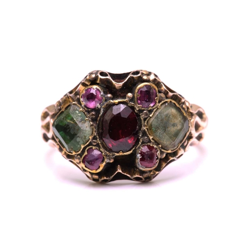247 - A gem-set dress ring in yellow metal, featuring an oval cut garnet in the centre flanked by two foil... 