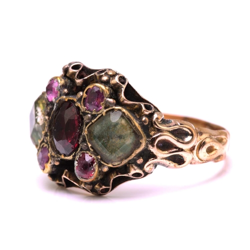 247 - A gem-set dress ring in yellow metal, featuring an oval cut garnet in the centre flanked by two foil... 