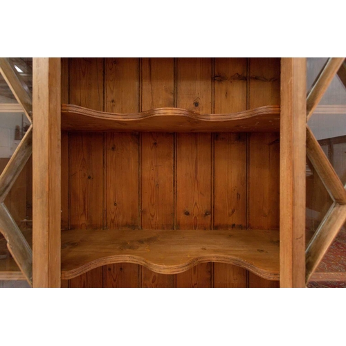 132 - An architectural stripped pine open cupboard bookcase with lattice glazed flanks above a pair of pan... 