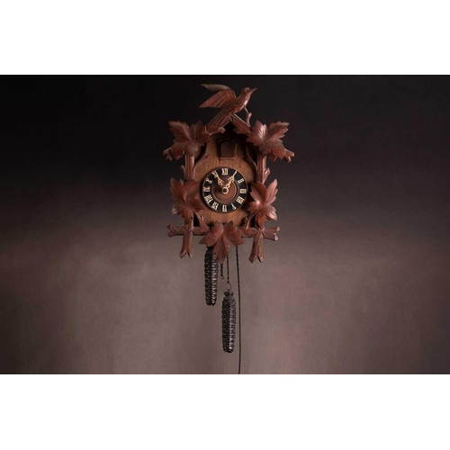 173 - An early 20th century carved walnut cuckoo wall clock with a pair of cast pine cone weights and leaf... 