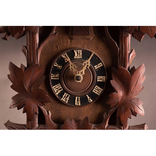 173 - An early 20th century carved walnut cuckoo wall clock with a pair of cast pine cone weights and leaf... 