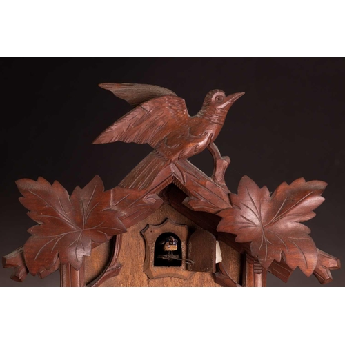 173 - An early 20th century carved walnut cuckoo wall clock with a pair of cast pine cone weights and leaf... 